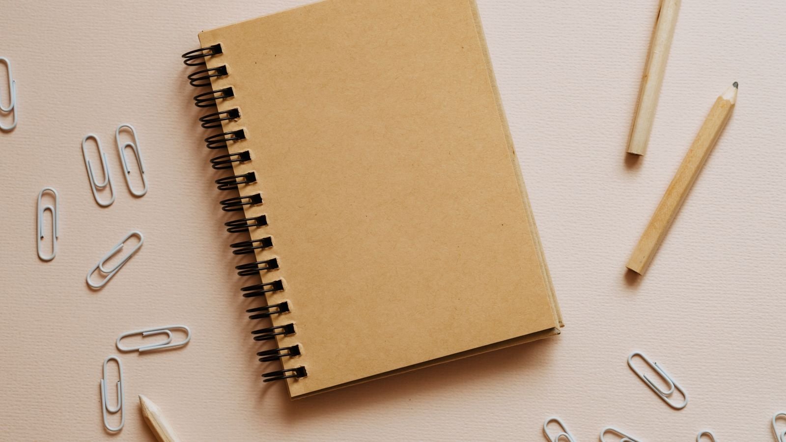 A minimalist flat lay of a spiral notebook, pencils, and erasers on a beige background, representing back-to-school planning
