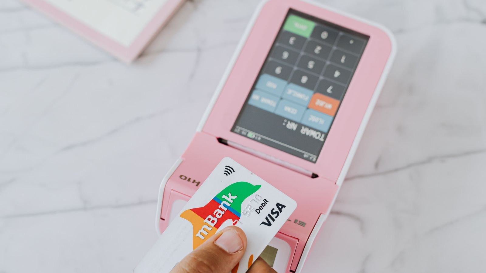 Close-up of hand swiping a card on a payment terminal, representing consumer debt and loan payment trends